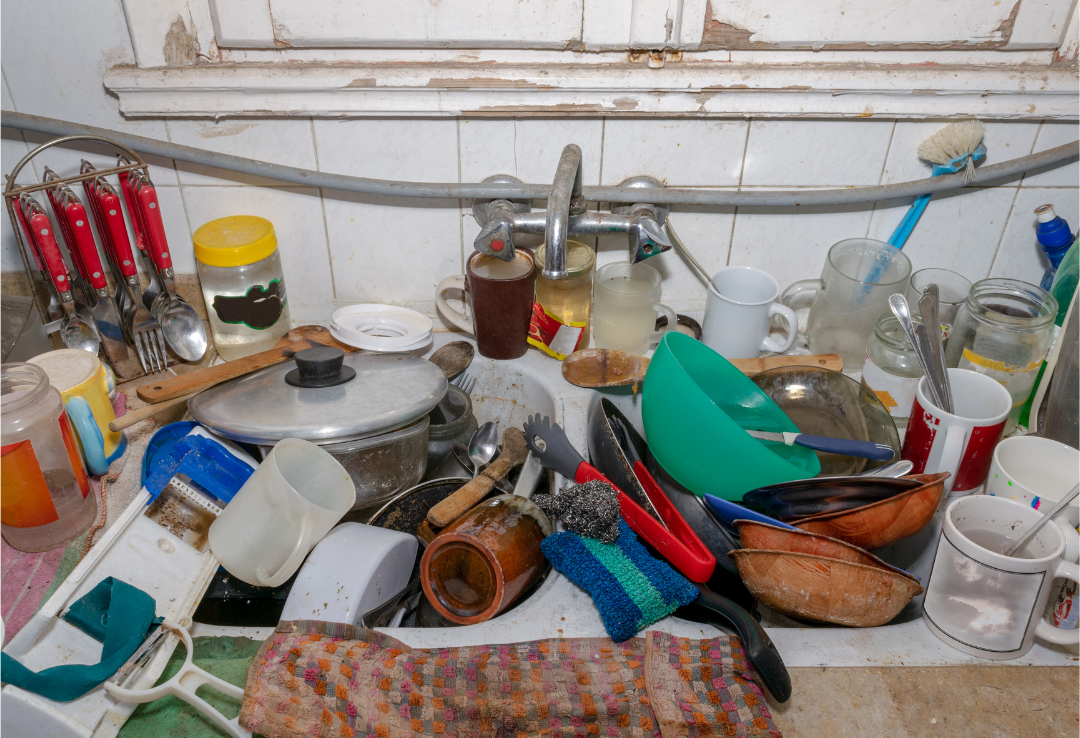 Évier rempli de vaisselle sale et désordre dans une cuisine, mettant en évidence les risques d'un environnement mal entretenu et la nécessité d'un nettoyage professionnel